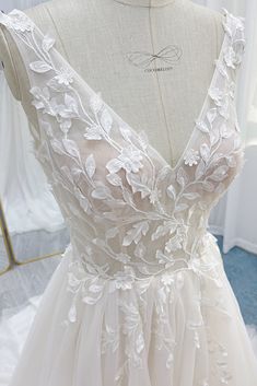 a wedding dress on display in front of a mannequin with white flowers and leaves