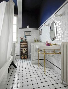 a white tiled bathroom with black and white tile flooring on the walls, along with a gold framed mirror