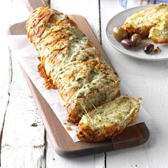 a loaf of bread sitting on top of a cutting board next to an olives