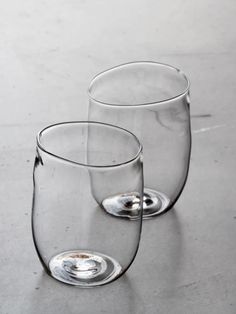 two empty wine glasses sitting on top of a gray table next to each other and one is half filled with water