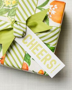 an orange and green gift wrapped in paper with the word cheers on it, sitting on a white surface