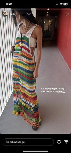 a woman wearing a multicolored crochet dress standing in front of a wall