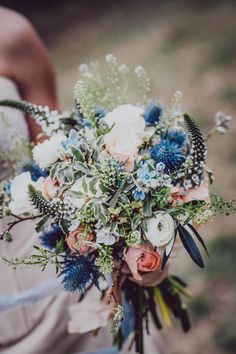 Bridal bouquet in peach, cream and blue tones being held by a bride. Eryngium Bouquet, Blue Roses Wedding Bouquet, Coastal Wedding Flowers, Scottish Wedding Dresses, Natural Bridal Bouquet, Wild Wedding Bouquet, Thistle Bouquet, Barefoot Bride, Wildflower Wedding Bouquet