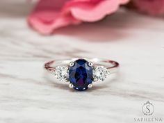 a blue and white diamond ring sitting on top of a table next to pink flowers