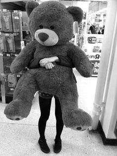 a woman is holding a large teddy bear in her arms while standing next to a store display