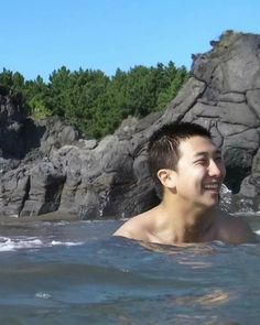 a young man swimming in the ocean next to some rocks