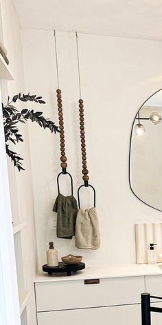 a white bathroom with two mirrors and hanging hooks on the wall next to a black chair