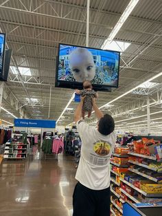 a man holding up a stuffed animal in front of two televisions at a store