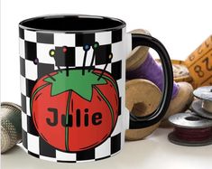 a black and white checkered coffee mug with a tomato on it, surrounded by thread spools