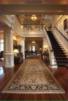 a large area rug in the middle of a room with stairs and chandelier