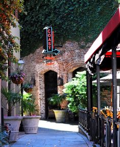 an alley way with tables and umbrellas on either side, in front of a brick building