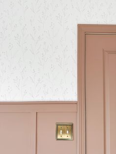 a pink door with a light switch in the corner and wallpaper on the walls