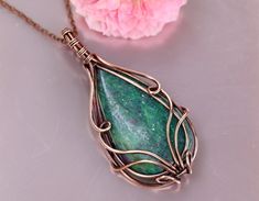 a necklace with a green stone hanging from it's side next to a pink flower