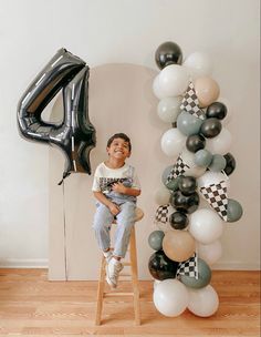 a young boy sitting on a stool in front of a number four balloon arch with black and white balloons