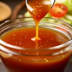 a spoon pouring honey into a glass jar filled with liquid and vegetables in the background