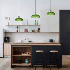 two stools sit in front of an island with three green lights hanging from it