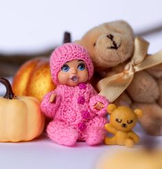 there is a small doll next to two teddy bears and pumpkins on the table