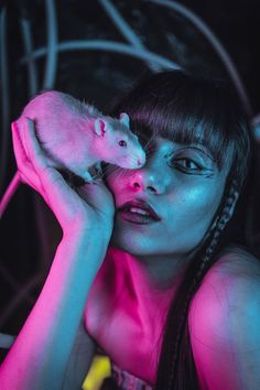 a woman holding a small rat in her right hand and looking at the camera with pink light on