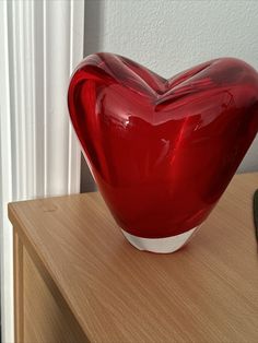 a red heart shaped vase sitting on top of a wooden table