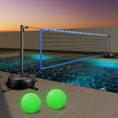 two green balls sitting next to a net on the side of a swimming pool at night