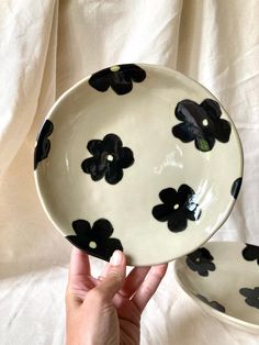 two black and white plates with flowers on them, one being held up by a hand