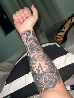 a man's arm with a clock tattoo on it, sitting on a bed