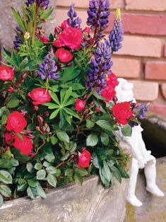 a planter filled with lots of flowers next to a statue on the side of a building