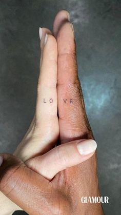 two hands holding each other with the word love tattooed on their thumbnails in front of them