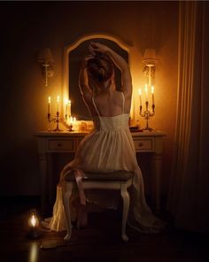 a woman sitting on a chair in front of a vanity with candles lit behind her