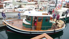 several people are standing on the deck of a green and white boat in a harbor