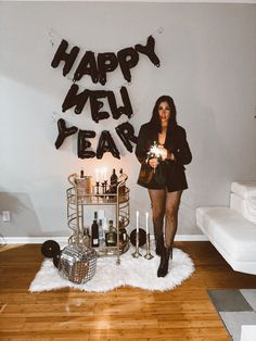 a woman standing in front of a happy new year sign with candles and wine bottles