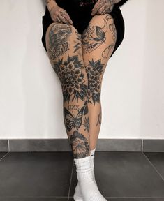 a woman with tattoos on her legs and knees sitting in front of a white wall