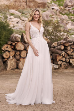 a woman in a white dress standing next to some rocks and trees with her hands on her hips