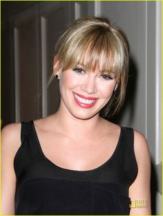 a woman with blonde hair smiling and wearing a black top, in front of a door