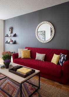 a living room with a red couch and coffee table in front of a gray wall