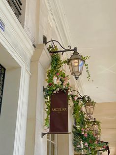 a sign hanging from the side of a building with flowers growing on it's sides