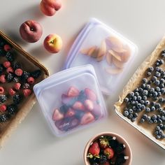 three plastic containers filled with fruit on top of a white table next to other food