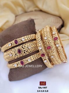 three gold bangles with red stones and pearls on the ends, sitting next to a pillow