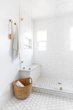 a bathroom with white tile and gold trim on the shower wall, along with a wicker basket