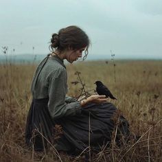 a woman sitting in the middle of a field with a bird on her lap and looking down