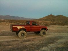 a red pick up truck driving down a dirt road