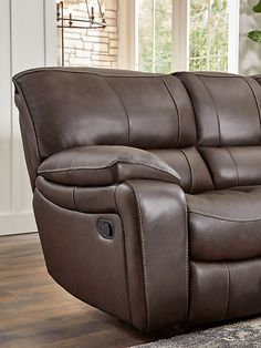 a brown reclining couch sitting on top of a wooden floor next to a window