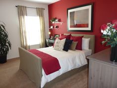 a bedroom decorated in red and white with flowers on the bed, potted plant