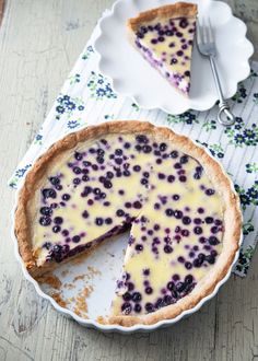 a blueberry cheesecake on a white plate with a slice missing from the pie