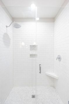 a walk in shower sitting next to a white tiled wall and floor with an overhead shower head