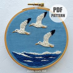 three seagulls flying over the ocean in blue and white embroidery on a hoop