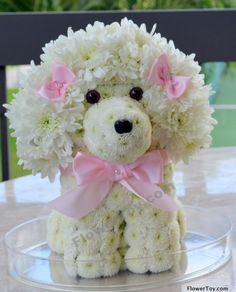 a white teddy bear sitting on top of a table next to a glass bowl filled with flowers