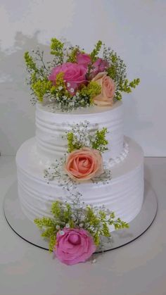 three tiered wedding cake with pink and orange flowers on the top, sitting on a white table