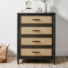 a black and brown dresser with wicker drawers next to a basket on the floor