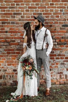 a man and woman standing next to each other near a brick wall with flowers in their hair